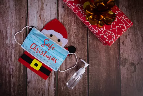 Santa Claus with medical face mask, sanitizer and gift box on wooden background