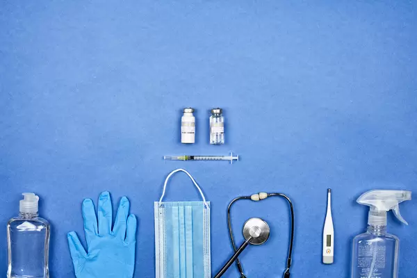 Sars-CoV-2 vaccine doses, face mask and medical equipment on blue background with copy space