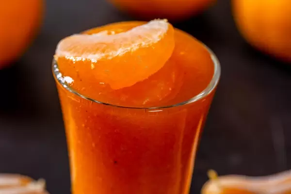 Sattoranger Smoothie aus Mandarinen und Kaki, dekoriert mit Mandarinenschnitz vor dunklem Hintergrund