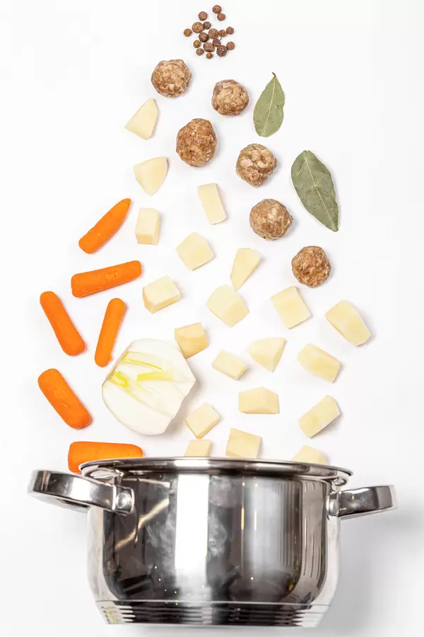 Saucepan with meatballs, vegetables and spices on a white background