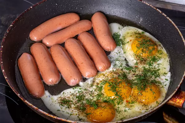 Sausages and fried eggs in a frying pan with spices and herbs