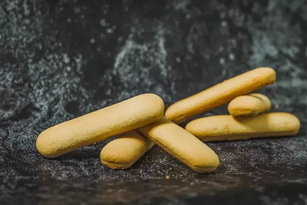 Savoiardi or ladyfingers cookies on pink plate on gray background, side view. Close-up. (Flip 2019)