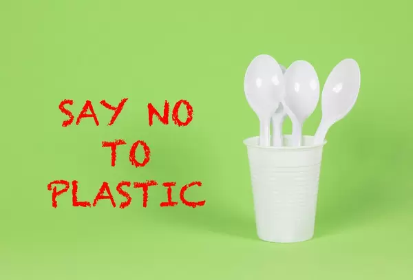 Say No To Plastic - Plastiklöffel im Becher auf grünem Hintergrund