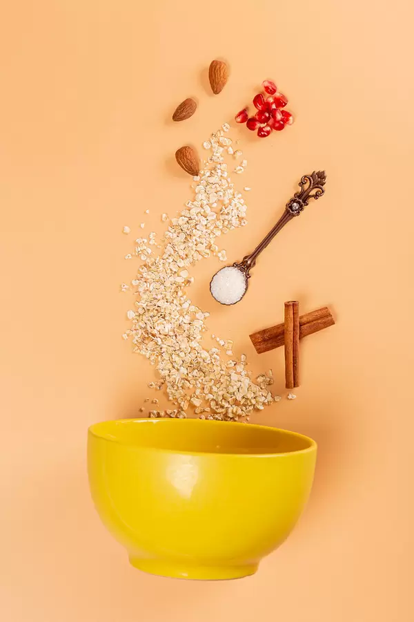 Scattered oatmeal with almonds, pomegranate, cinnamon and a spoonful of sugar on a yellow background with a bowl. Breakfast ingredients