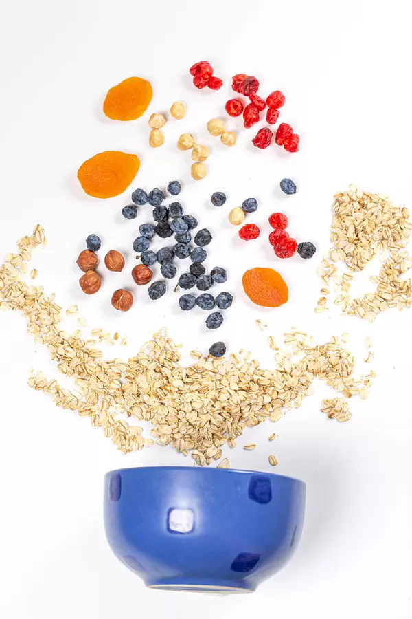 Scattered oatmeal with dried fruit, nuts and a blue bowl. Healthy breakfast concept