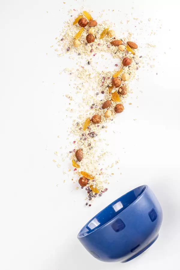 Scattered oatmeal with dried raspberries, blackberries, raisins and nuts with a blue bowl, top view