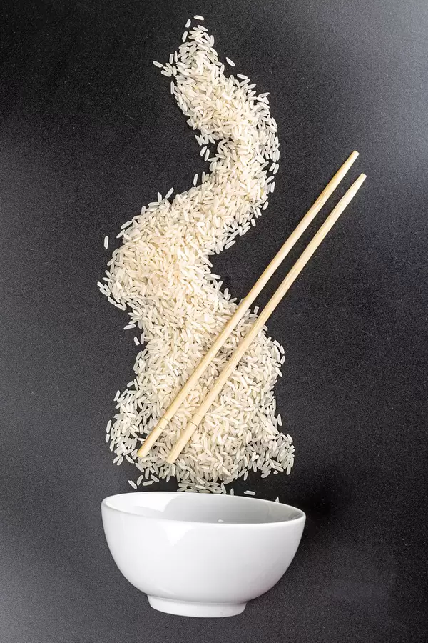 Scattered raw rice with wooden chopsticks and white bowl on black background
