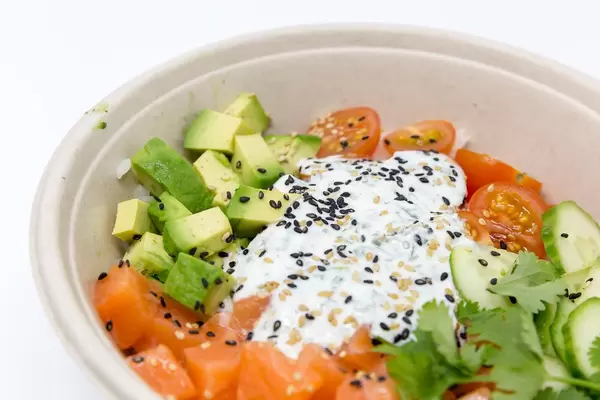 Schale mit geschnittenen Tomaten, Avocado, Gurken, verfeinert mit Petersilie, Joghurt und gesunden Samen