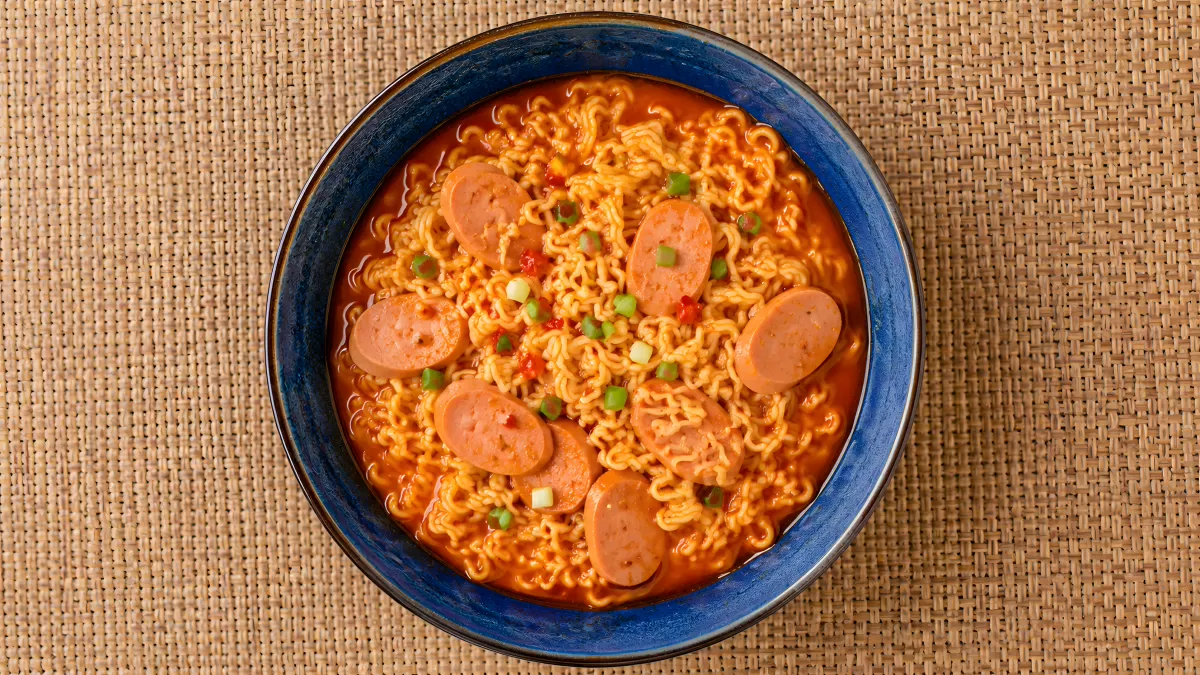 Scharfe Ramen-Suppe mit Würstchen in blauer Schüssel