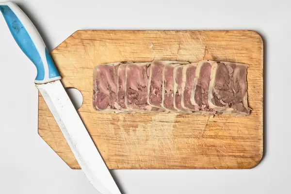 Scheiben von geräucherter Rinderzunge mit einem Messer auf einem Holzbrett. Aufnahme von oben