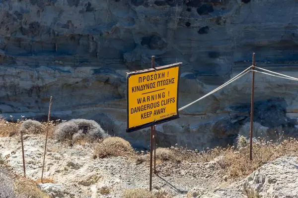 Schild auf Griechisch und Englisch warnt Touristen vor Gefahr auf der Klippe in Papafrangas auf Milos