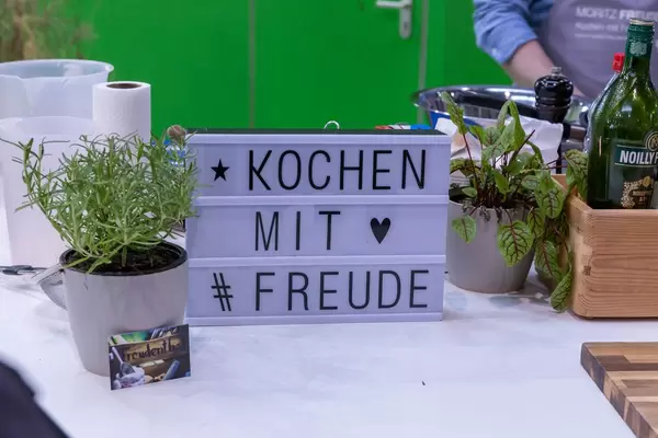 Schild mit Aufschrift Kochen mit Freude zwischen Gartenkräutern und Gewürzen
