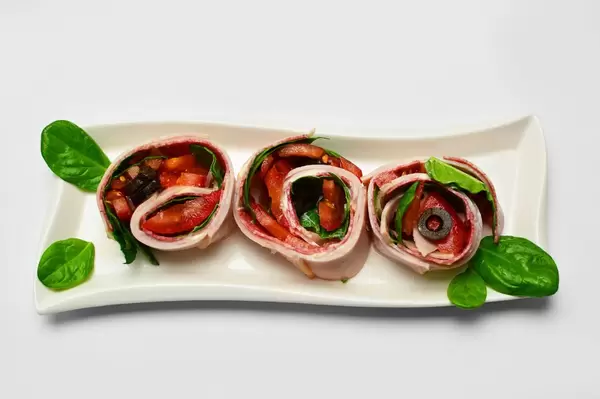 Schinken-Gemüse Röllchen mit Tomaten und Oliven in der Aufsicht