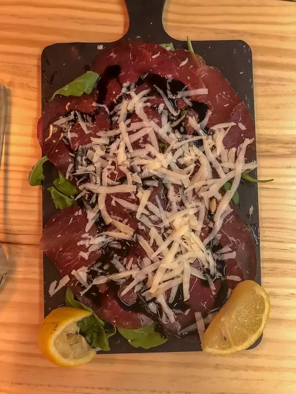 Schinken mit geriebenem Parmesan Käse auf Rucolabett mit Zitrone und Balsamico Essig auf einem schwarzen Brettchen