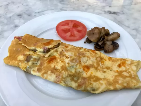 Schinken-Pilz Omelette mit Pilzen und einer Scheibe Tomaten auf einem weißen Teller