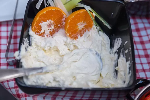 Schlagsahne, mit Orangenscheiben dekoriert, in einer schwarzen Schale auf einer rot-weiß-karierten Tischdecke