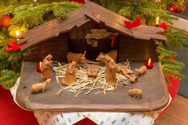 Schlichtes Krippenspiel mit geschnitzten Holzfiguren vor Weihnachtsbaum