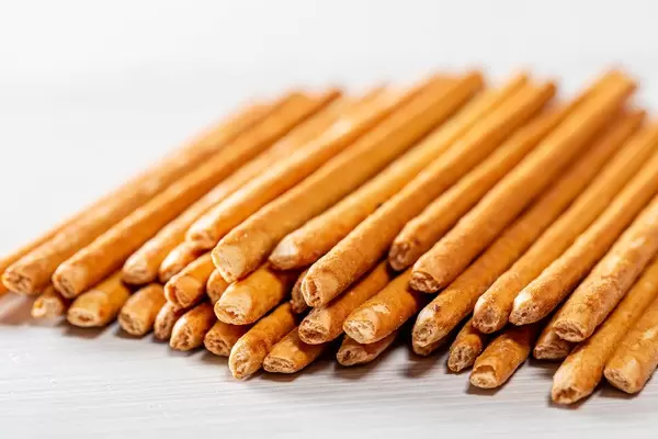 Schmackhafte Apero-Cracker in Stäbchenform liegen auf weißem Holztisch