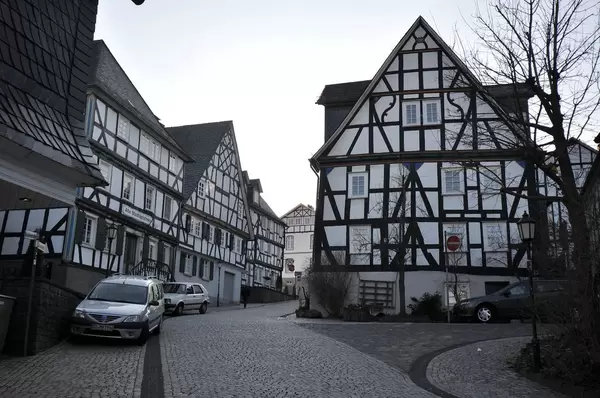 Schmale mit Basaltsteinen gepflasterte Straße mit geparkten Autos zwischen weißen Fachwerkhäusern