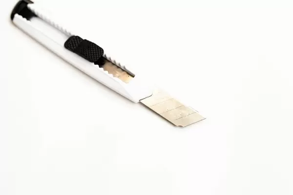 Schmales weißes Teppichmesser mit ausgefahrener Klinge freigestellt vor weiß