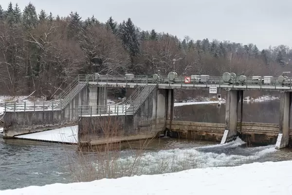 Schneebedeckter Staudamm für Fluss im Winter, im Hintergrund Wald