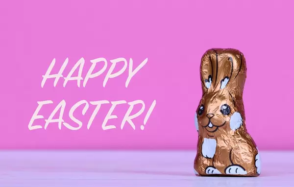 Schokoladen-Osterhase neben Text Happy Easter mit rosa Hintergrund