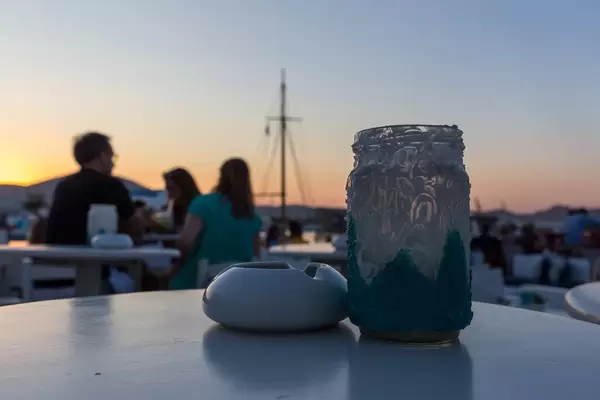 Schön verziertes Kerzenglas neben Aschenbescher vor Sonnenuntergang am Hafen von Paros