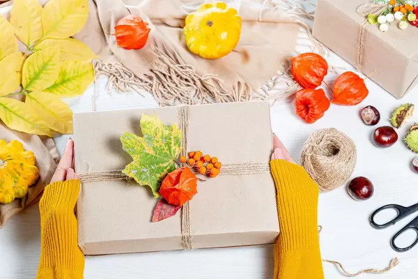 Schönes, herbstlich handverpacktes Geschenk in den Händen einer Frau als Symbol für Familienzeit zu Thanksgiving