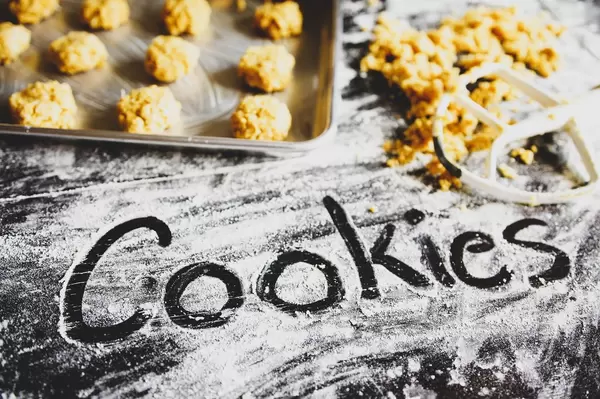 Schriftzug COOKIES in Mehl geschrieben, daneben Backbleck mit noch rohem Gebäck und Teigresten