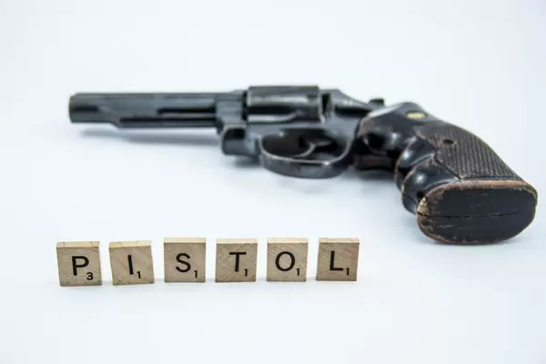 Schriftzug PISTOL mit Buchstaben auf Holzplättchen vor Revolver auf weißem Hintergrund