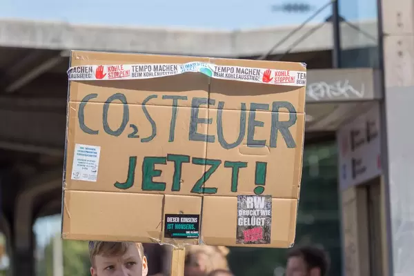 Schüler schaut bedenklich und hält das Schild "CO2 Steuer jetzt" in die Luft