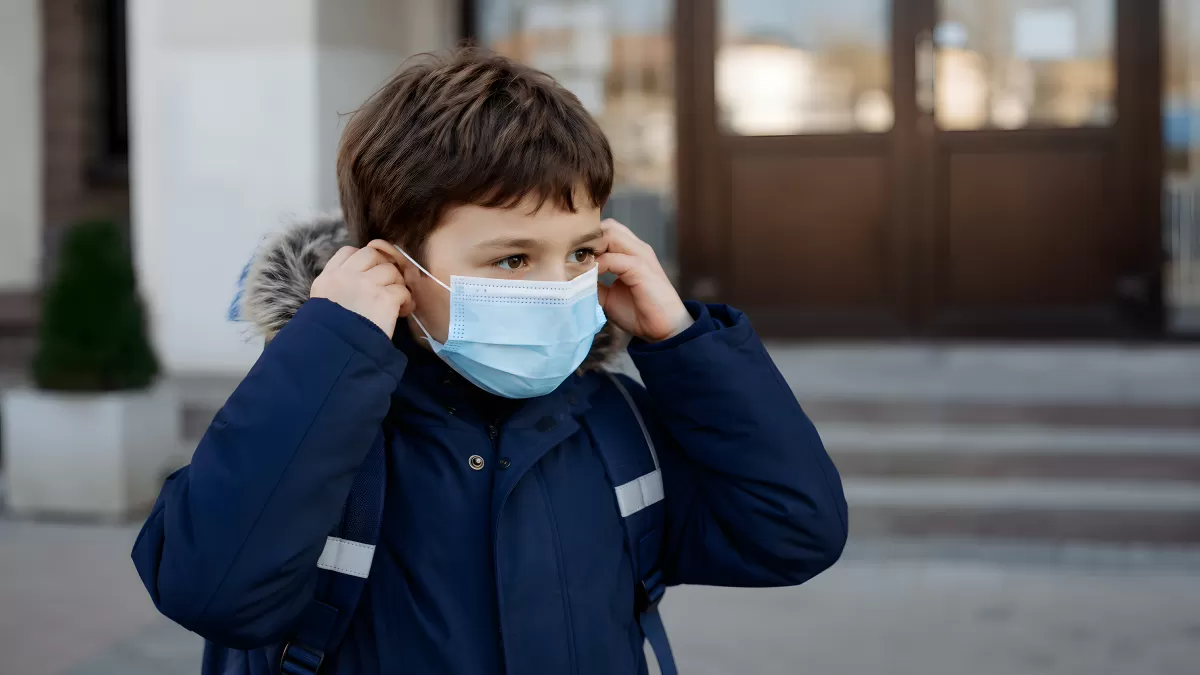 Schulkind setzt Atemschutzmaske vor Schulgebäude auf