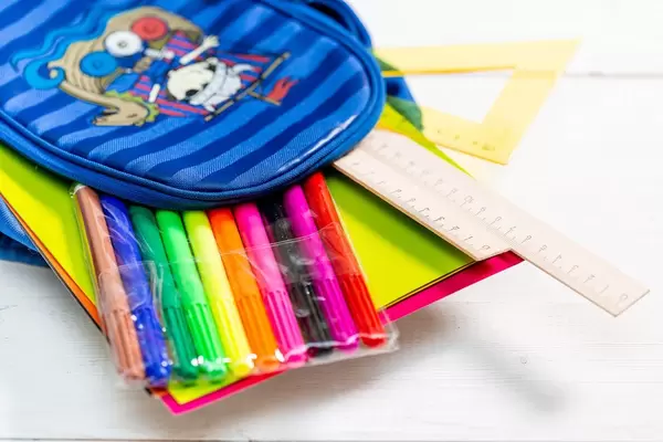 Schultasche mit bunten Stiften, Bastelpapier und Lineal vor weißem Hintergrund