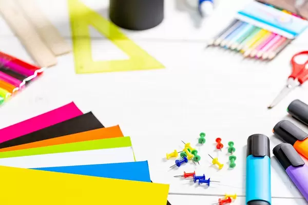 Schulutensilien wie Lineal, Buntstifte, Pinnadeln, Textmarker, Schere, bunte Papierbögen auf Bürotisch