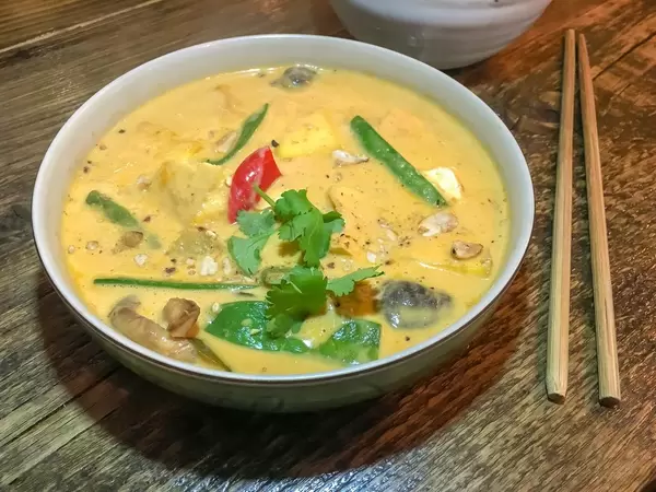 Schüssel mit Curry mit Pilzen, Bohnen und Petersilie neben Essstäbchen auf Holztisch