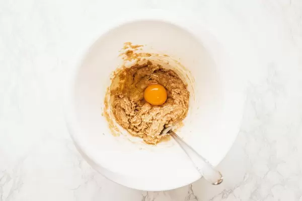 Schüssel mit Zutaten für Plätzchenteig und rohem Ei auf mit Mehl bedecktem Tisch