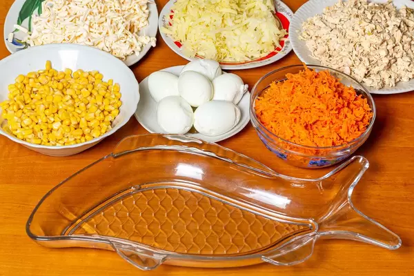 Schüsseln und Teller mit Mais, Eiern, geriebenen Karotten, Kohl, Käse und Thunfisch auf einem Tisch