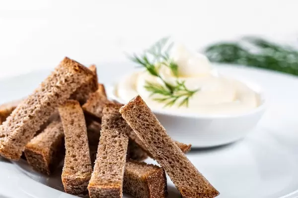 Schwarzbrot-Cracker vor verschwommener weißer Sauce mit Dill