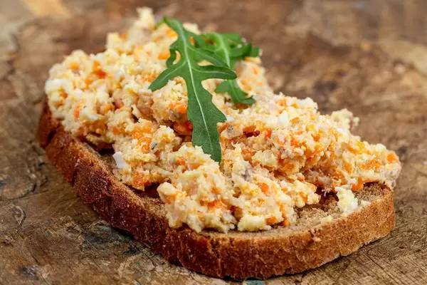 Schwarzbrot-Scheibe mit Rührei und Rucola belegt auf einem Holzbrett Nahaufnahme