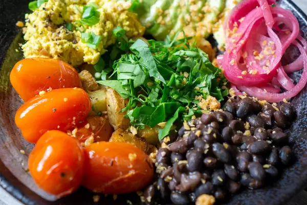 Schwarze Bohnen, Kirschtomaten, Rührei, Bratkartoffeln und Kräuter auf einem Teller als gesunde Mahlzeit Nahaufnahme