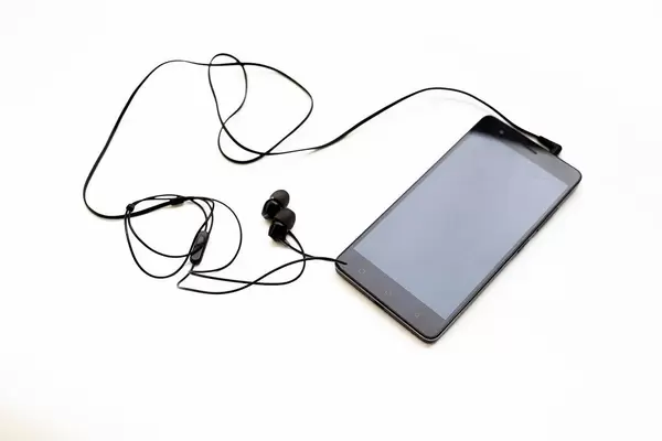 Schwarze Kopfhörer eingesteckt in Mobiltelefon mit ausgeschaltetem Bildschirm vor weißem Hintergrund