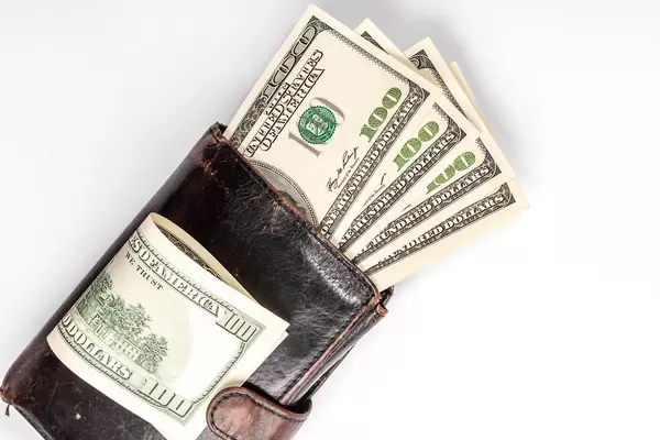 Schwarze Leder-Geldbörse mit Geld gefüllt und Dollar-Scheinen darauf, vor weißem Hintergrund