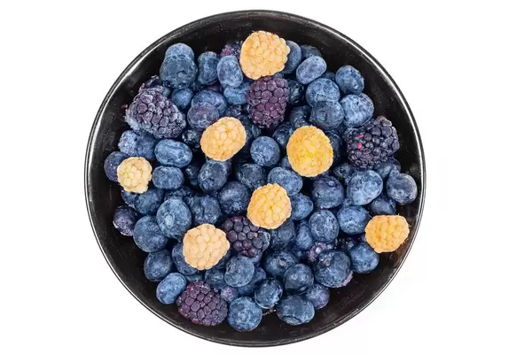 Schwarze Schale mit gelben Himbeereen, Maulbeeren und Blaubeeren auf weißem Hintergrund von oben fotografiert