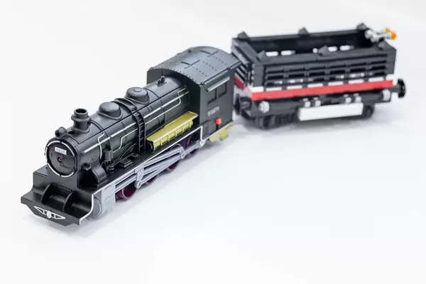 Schwarze Spielzeuglokomotive mit Anhänger, auf weißer Oberfläche