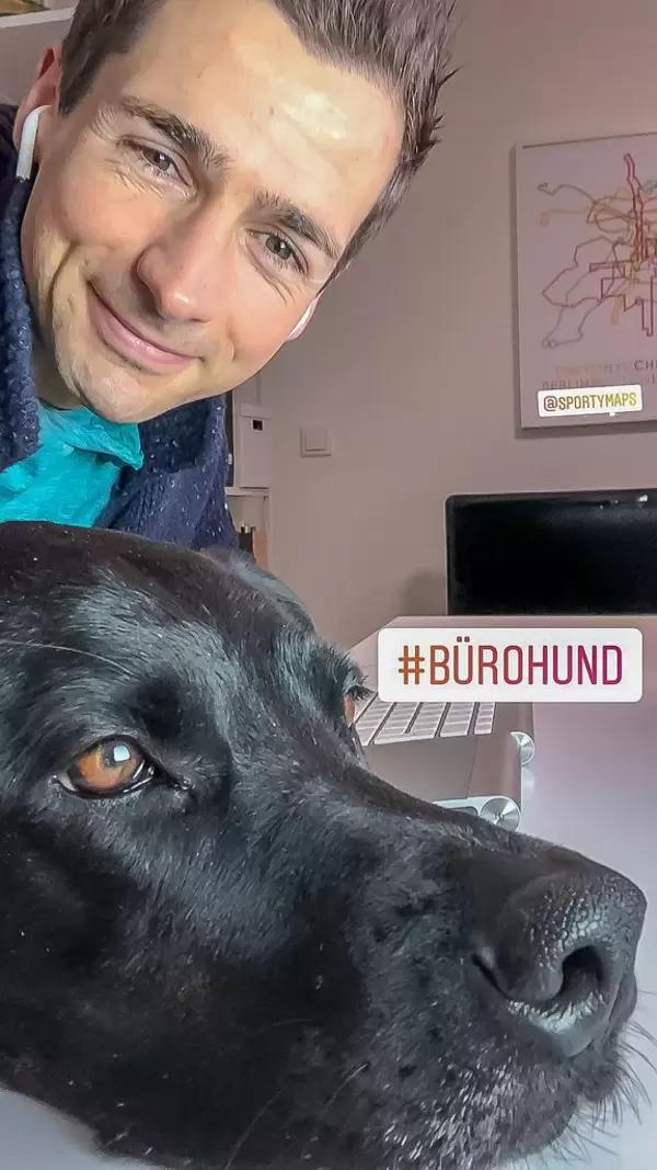 Schwarzer Bürohund legt Kopf auf Schreibtisch mit Tastatur an dem Mann arbeitet