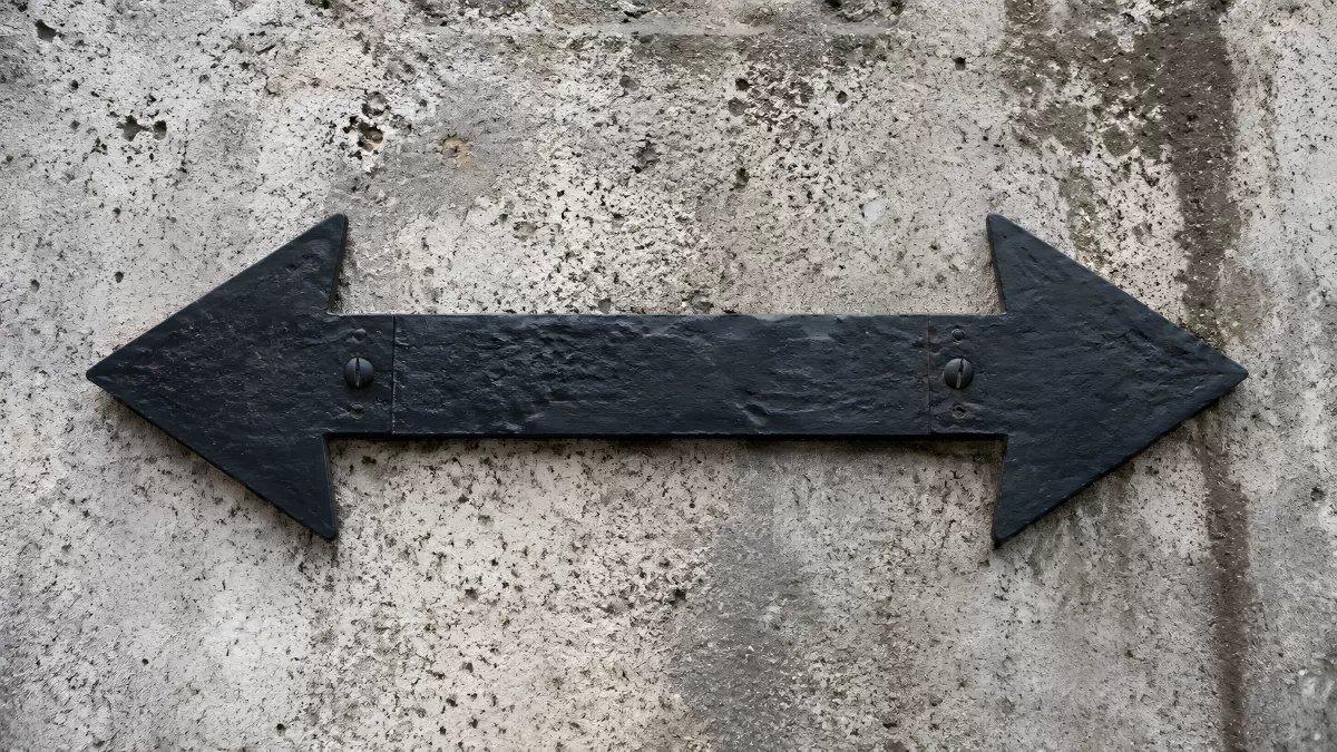 Schwarzer Doppelpfeil aus Metall an Betonwand