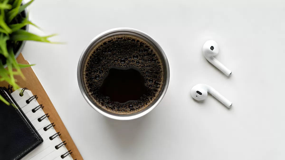 Schwarzer Kaffee mit AirPods und Notizbuch von oben