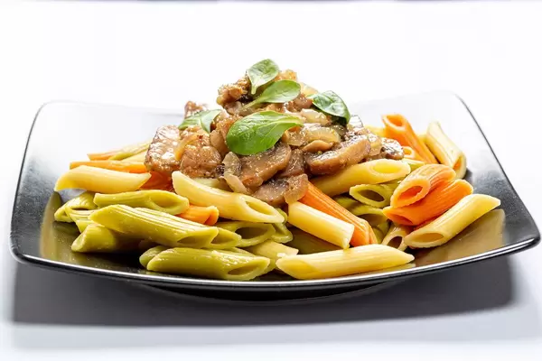 Schwarzer Teller mit bunten Nudeln, Fleisch und Pilzen