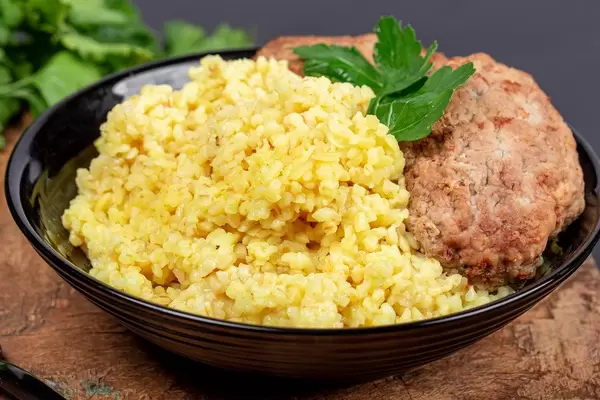 Schwarzer Teller mit Weizen-Porridge, frischer Petersilie und Hackbraten auf einem Holzschneidebrett Nahaufnahme