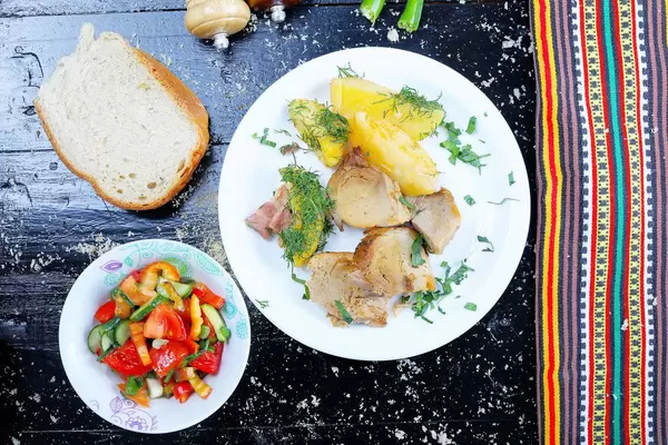 Schweinebraten mit Brot und gemischtem Gemüsesalat auf einem schwarzen Hintergrund